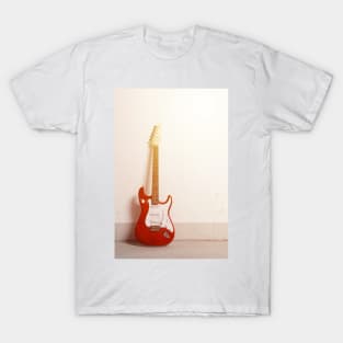 Red electric guitar standing left against white raw wall T-Shirt